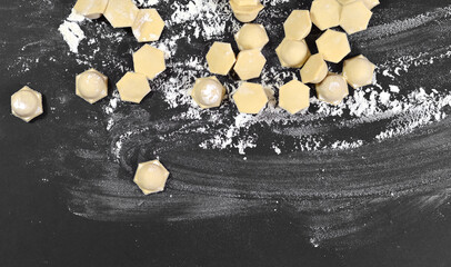 Dumplings, ravioli on a black table sprinkled with wheat flour. There are many small pieces of...