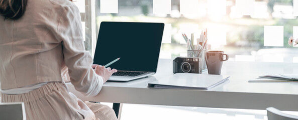 Cropped shot of young businesswoman working on laptop computer while sitting at her office desk, panoramic view.