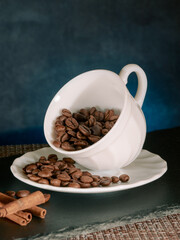 Coffee roasted beans with cinnamon sticks in white ceramic mug blue background