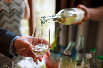 The waiter holds a bottle of champagne in his hand and pours it into a glass.