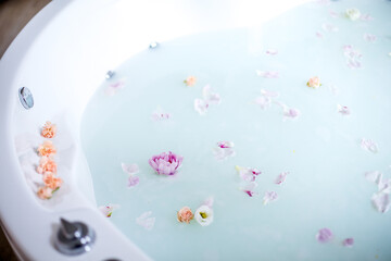 Fototapeta na wymiar Relaxing bath with milk, flowers and rose petals. Bright room, romantic, relaxing atmosphere.
