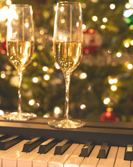 Champagne glasses on piano keyboard with Christmas lights on background. Holidays, Christmas, Happy New Year concept, vertical banner