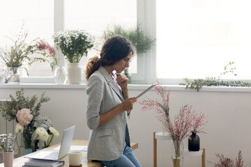 Think twice before doing. Pensive young lady florist look on gadget screen thinking on client question. Designer having doubt in accepting supplier offer or planning work considering customer demand