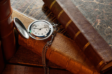 Vintage pocket watch with chain and antique books on a wooden table close-up.