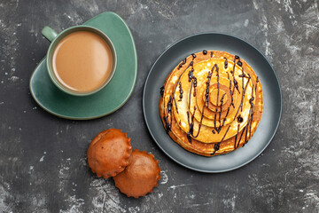 Overhead view of delicious pancake with two cakes on black plate with a cup of coffee on gray background