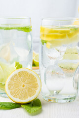 Close-up of two glasses of ice water, half a lemon and mint leaves, on white table, in vertical