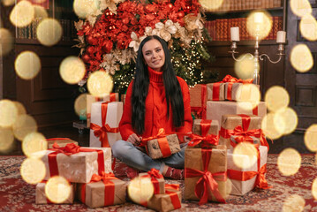 woman in a knitted sweater with New Year's gifts in the New Year's studio. The happy girl opens the gift. bokeh