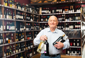 Joyful elderly man with bottles of wine at the liquor store.