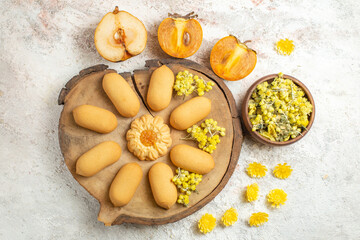 cookies on woofen platter and fruits and different yellow flowers around it on marble background