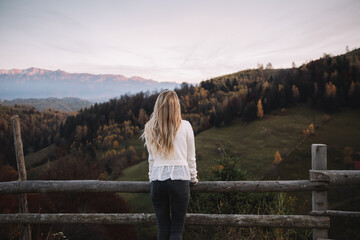 Traveler female standing near the fence and watching the sunset in the autumn mountains.