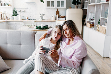 mom and daughter sit on the couch and watch a movie on the phone, watch social networks, chat with friends