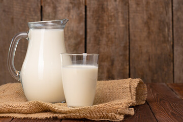 Glass pitcher of milk on old wooden table