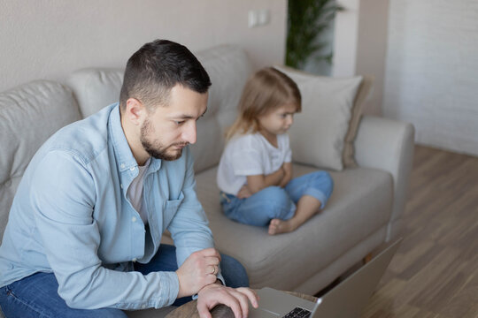 No Time For Child. Dad busy with laptop, working online at home, sad bored offended daughter sitting nearby, free space.Family a businessman father working at a computer and his child angry.