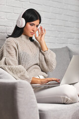 Beautiful young woman working on laptop while sitting on sofa in living room at home.