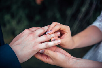 Bride putting gold wedding ring on groom's finger during wedding ceremony, close up, blurred background.