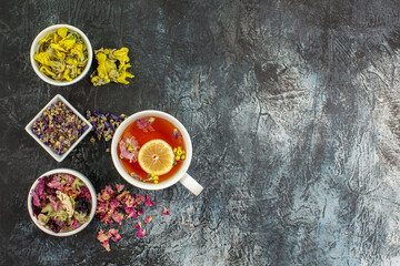 overhead shot of a cup of herbal tea with bowls of dry flowers on the left side of grey background