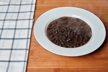 White plate with black beans on a wooden board
