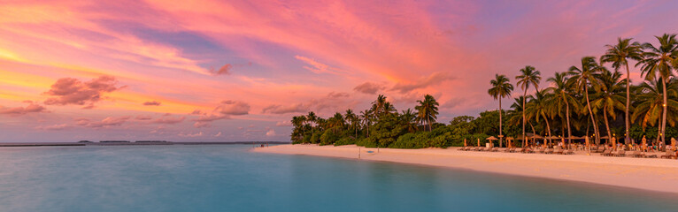 Tropical beach panorama sunset summer sky. Panoramic beach landscape. Resort beach and seascape. Orange and golden sunset sky, soft sand palm trees, calmness, tranquil relaxing sunlight. Luxury travel