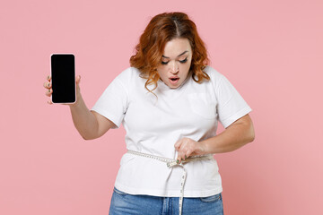 Shocked young redhead plus size body positive woman 20s in white t-shirt hold mobile cell phone...
