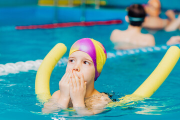 A little boy with a life jacket on his chest learns to swim in an indoor pool.