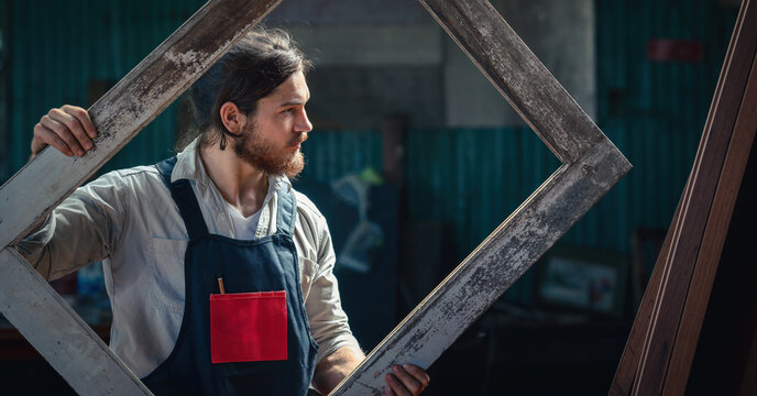 carpenter in wood workshop selecting wooden frame for his workwood