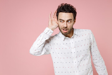 Shocked curious young bearded man 20s wearing basic casual white shirt standing try to hear you...