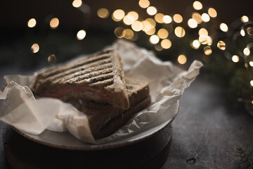 Sandwich on a plate surrounded by New Year's lights and pine. Food on a dark background. Christmas mood in a cafe