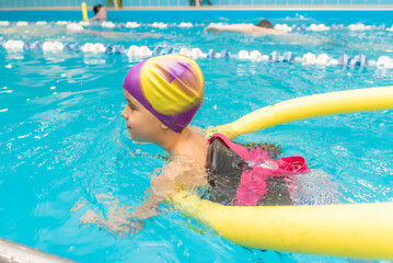 A little boy with a life jacket on his chest learns to swim in an indoor pool.
