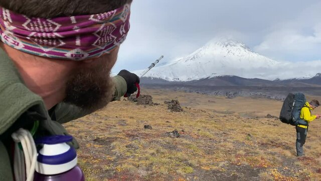 A seasoned beard and a traveler with a large backpack shows the sign of peace and victory with the fingers of both hands. A group of tourists in Kamchatka.