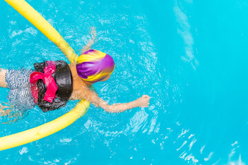A little boy with a life jacket on his chest learns to swim in an indoor pool.