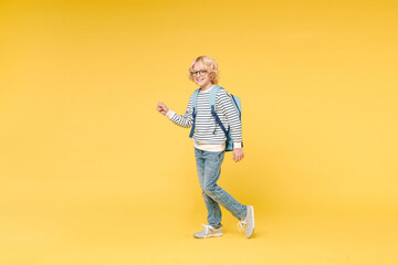 Full length side view of smiling male boy 10s years old in striped sweatshirt eyeglasses backpack...