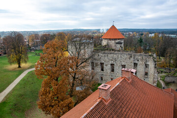 Cesis, Latvia - Top view of the tiled roof and medieval stone castle, trees in autumn on green grass, gray sky during the day.