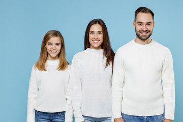 Smiling young happy parents mom dad with child kid daughter teen girl in basic white sweaters looking camera isolated on blue color background studio portrait. Family day parenthood childhood concept.