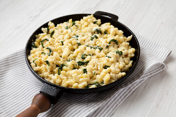 Homemade Spinach Mac and Cheese in a cast-iron pan on a white wooden background, side view.