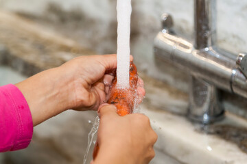 Little girl washes carrot in marble sink in kitchen. Fresh healthy food for small kid