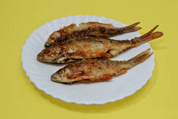 Three friend fish lie on white plate on yellow background