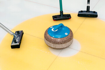 Brooms and stone for curling. view of blue curling stone in outer blue ring of house with broom...