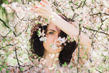 Young attractive woman with curly long hair posing in spring blooming garden, apple trees