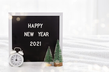 Blackboard with the words Happy New Year 2021 on bed next to white clock for 12 hours and mini Christmas trees. Home interior. New Year and Christmas at home. Space for text. Bokeh lights