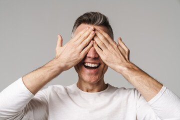 Smiling man covers eyes with hands isolated