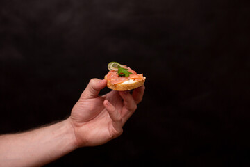 a man's hand on a black background holds a sandwich with a red fish