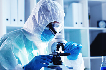 Medical worker in protective gown looking in microscope