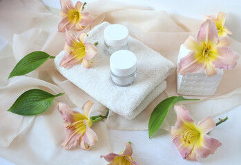 Fototapeta na wymiar Terry towel with body care products among the delicate flowers of the daylily, top view - the concept of gentle body care