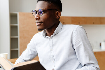 Afro american focused man in eyeglasses reading book