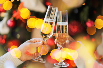 two glasses of champagne are clinked by a couple on a holiday. new year lights glow brightly with the rays from the garland. background texture of Christmas lights on a holiday tree. make a wish.