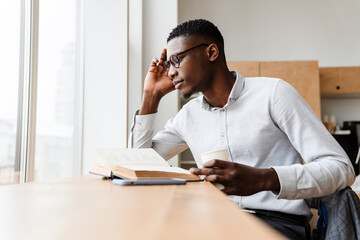 Afro american focused man reading book and drinking coffee