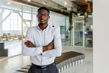 Afro american young man in eyeglasses and earphones standing indoors