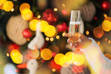 holding a glass in his hand against the background of a Christmas tree. Celebrates the holiday alone. Christmas lights are bright glow on the background