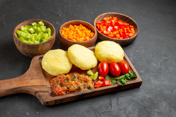 Close up view of uncooked vegetables on a cutting board and chopped foods on the black background