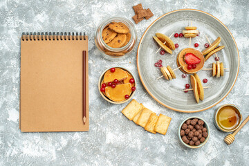 Homemade pancakes with fruit biscuits and honey next to notebook on blue background